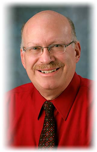 Man in red shirt, maroon tie and glasses. Smiling at camera