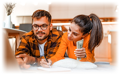 Man and woman laying on floor in front of a laptop, woman taking notes and holding cash, creating a budget